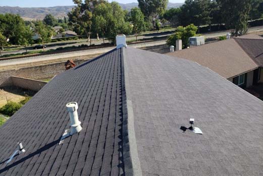 Roofer builder worker with nailgun installing Asphalt Shingles or Bitumen Tiles on a new house under construction